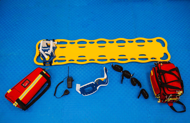 Bovenaanzicht van medische apparatuur, brancard, tas en verbanddoos op een blauwe achtergrond - Foto, afbeelding