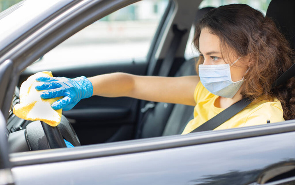 Woman in the car with protective glove and facial mask. Hands with blue gloves. She disinfecting and cleaning car  - Foto, immagini