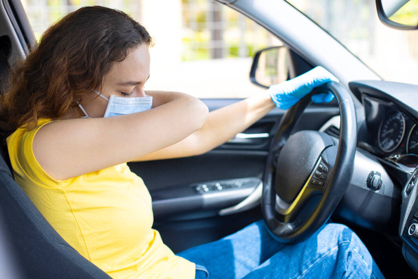 Young woman with face mask sneezing into elbow in the car - Photo, image