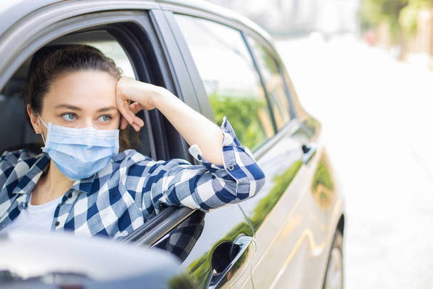 Young woman in a mask sitting in a car, protective mask against coronavirus, driver on a city street during a coronavirus outbreak. - Foto, Bild
