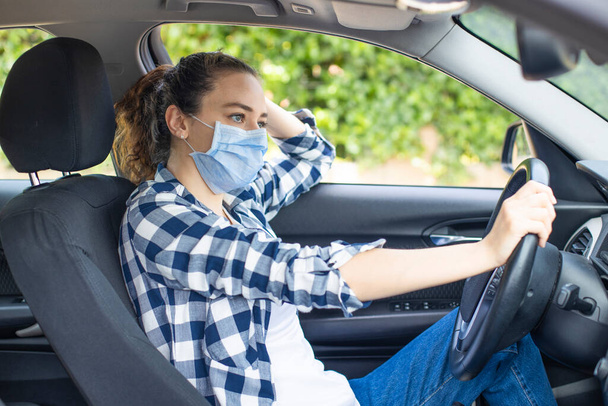 Young woman in a mask sitting in a car, protective mask against coronavirus, driver on a city street during a coronavirus outbreak. - Foto, Imagen