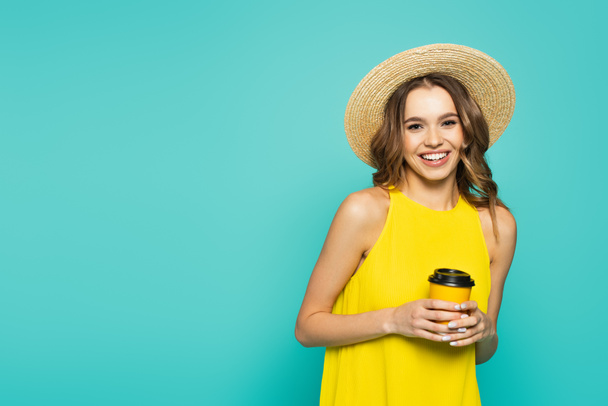 Fröhliche Frau in gelbem Kleid und Sonnenhut mit Kaffee to go auf blauem Grund  - Foto, Bild