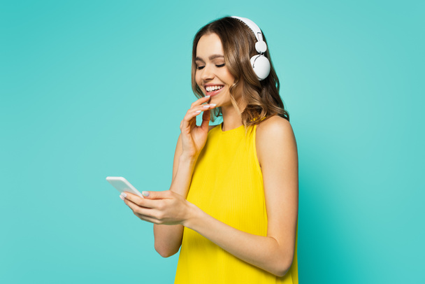 Smiling woman in headphones using smartphone isolated on blue  - Photo, Image