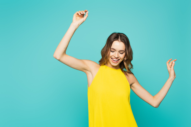 Cheerful woman in yellow dress dancing isolated on blue  - Фото, изображение