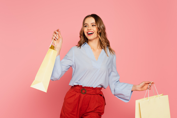 Happy woman holding shopping bags isolated on pink  - Фото, изображение