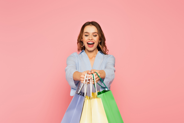 Excited shopaholic holding shopping bags isolated on pink  - Fotografie, Obrázek