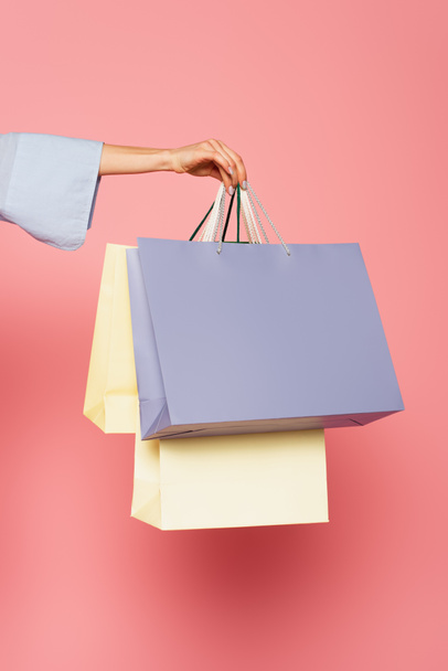 Cropped view of female hand holding shopping bags isolated on pink  - Foto, immagini