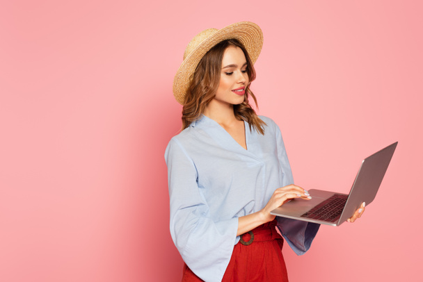 Stylish woman in sun hat using laptop on pink background  - Photo, Image