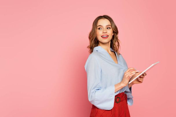 Smiling woman holding digital tablet on pink background  - Zdjęcie, obraz