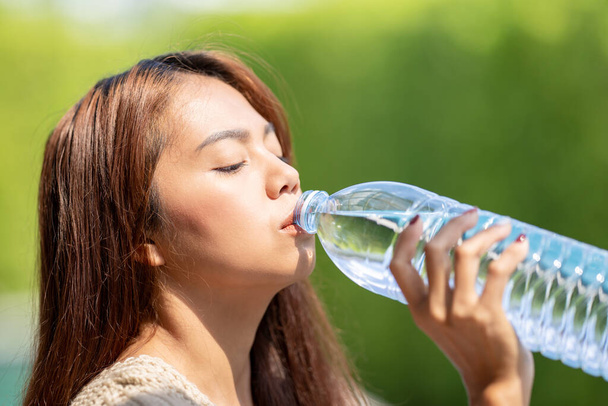 Asian Woman drinks big bottle water in outdoor green bokeh tree background. - Фото, зображення