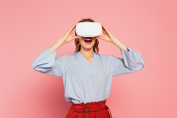 Amazed woman gaming in virtual reality headset on pink background  - Valokuva, kuva