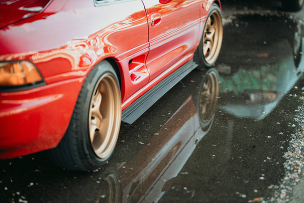 Uma vista lateral de um carro esporte cupê vermelho com a reflexão sobre o asfalto molhado - Foto, Imagem