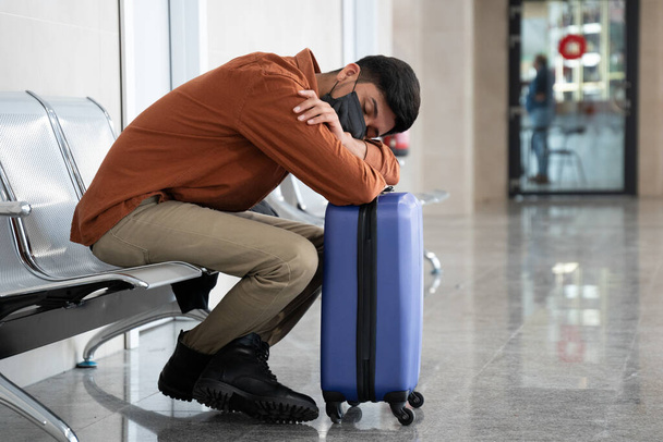 A closeup of a person in a facial mask at the airport sleeping on his luggage - a new normal concept - Foto, Imagem