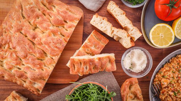 An overhead shot of Genovese focaccia bread with ingredients on a wooden table - Photo, image