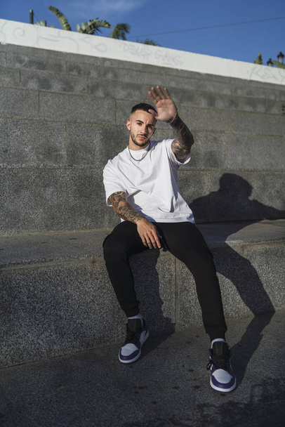 A Spanish man with tattoos in casual style sitting on stairs - Photo, Image