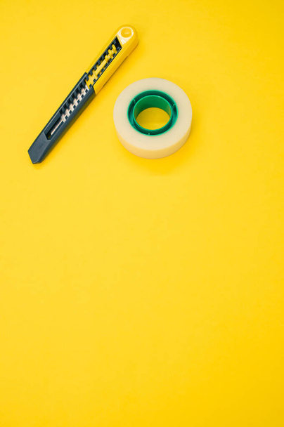 A closeup shot of an adhesive tape and a utility knife on a yellow background - Fotografie, Obrázek