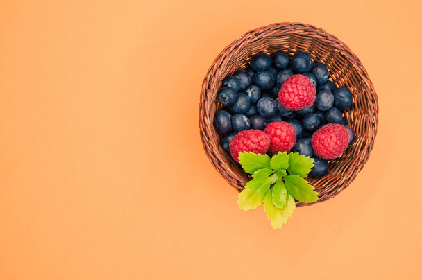 A top view of blueberries raspberries and leaves in a basket - Fotó, kép