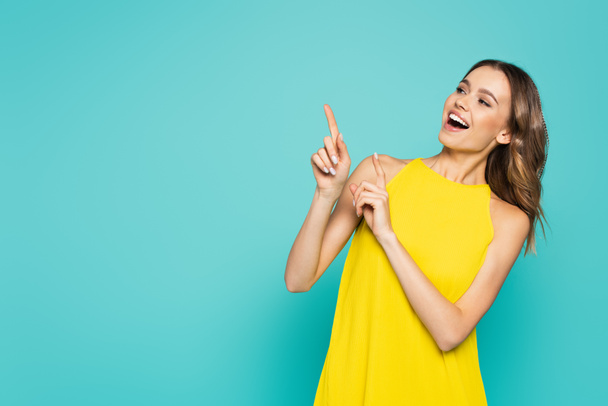 Smiling woman in yellow dress pointing with fingers isolated on blue  - Photo, image