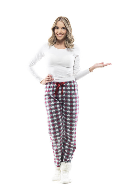 Glückliche süße junge Frau im Pyjama zeigt leeren Raum mit offener Hand. Volle Körperlänge isoliert auf weißem Hintergrund. - Foto, Bild