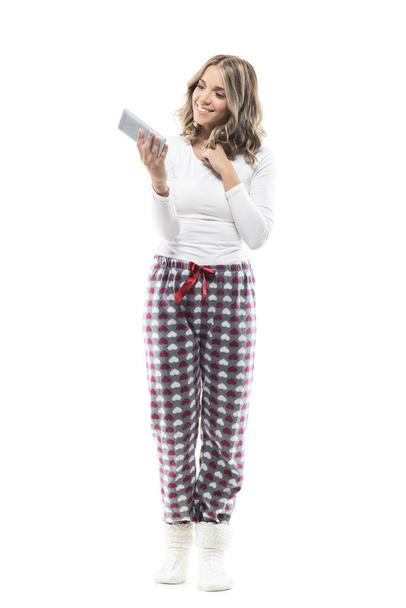 Juguetón femenino adorable joven belleza en pijama usando el teléfono celular. Longitud total del cuerpo aislado sobre fondo blanco. - Foto, imagen