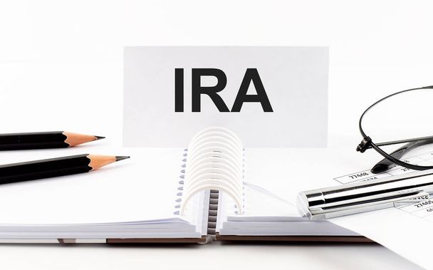 Text IRA on paper card,pen, pencils,glasses,financial documentation on the table - business concept - 写真・画像