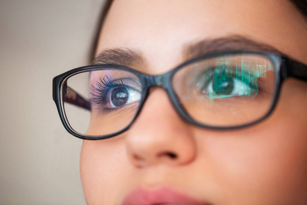 Nahaufnahme einer jungen Frau mit braunen Augen und Brille, die vor grauem Hintergrund wegschaut - Foto, Bild