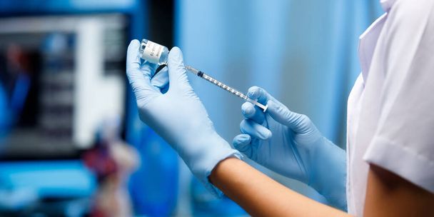 Pielęgniarka wyciągnąć butelkę szczepionki do strzykawki Dawka, Szczepienie dla odporności w niebieskim tonie szpitalnym pokoju. Covid-19 Koncepcje zdrowotne i medyczne - Zdjęcie, obraz