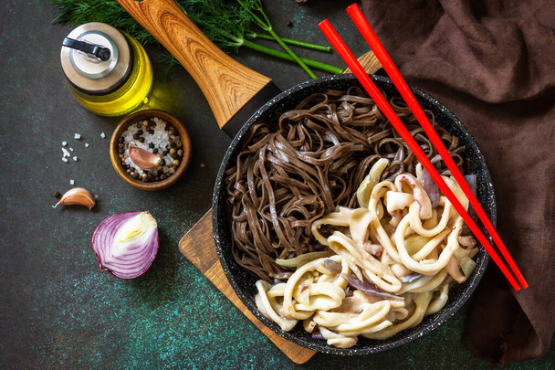 Spicy Noodles, Korean traditional food. Buckwheat soba noodles and squid with sour cream sauce on a dark stone table top. Top view flat lay background.  - 写真・画像