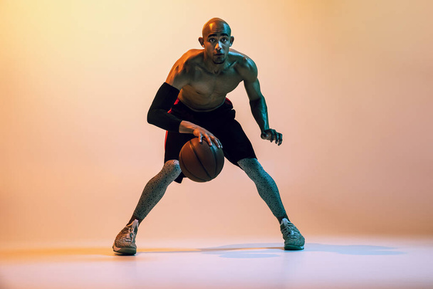 Portrait of african-american professional male basketball player in action in neon light on orange background. - Foto, imagen