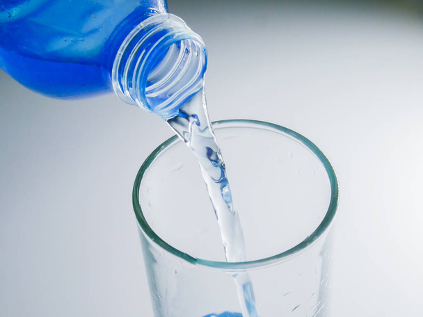 Ρίξτε καθαρό πόσιμο νερό από το μπουκάλι στο ποτήρι. - Φωτογραφία, εικόνα