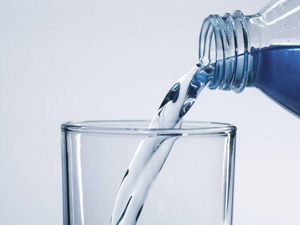 Giet schoon drinkwater uit de fles in het glas. - Foto, afbeelding