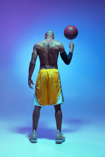 Sportive athletic african-american male basketball player posing in neon light on blue background. Rear view - Foto, Imagem