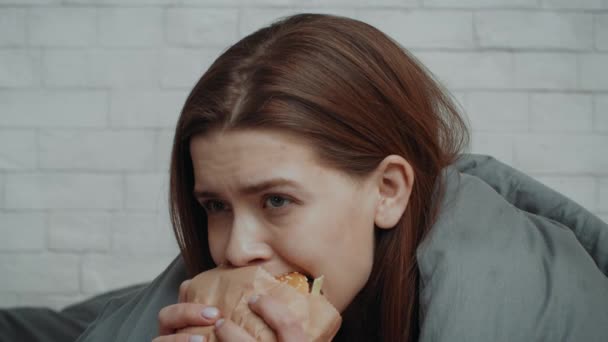 Mujer joven deprimida comiendo hamburguesa para consolarse en casa - Imágenes, Vídeo