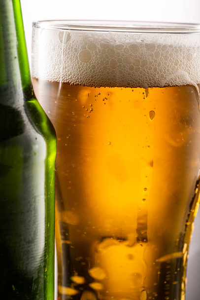 Beer glass and foam and green transparent bottle with beer beside - Foto, afbeelding