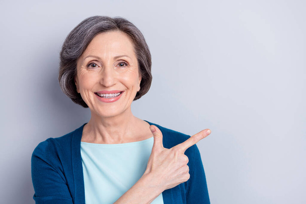 Photo portrait of smiling happy elder woman pointing finger copyspace recommending isolated on grey color background - Foto, Imagen