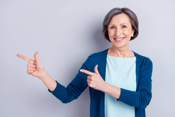 Photo of charming positive happy old woman point fingers empty space isolated on grey color background - Φωτογραφία, εικόνα