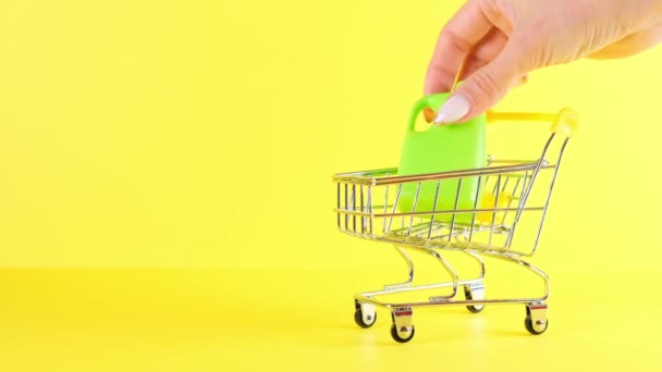 Shopping cart with bottles inside on a yellow background, closeup. Black Friday Shopping and Discount Concept - Footage, Video