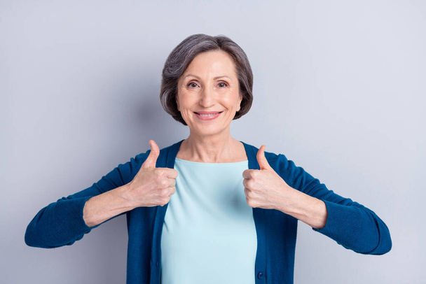 Photo of charming sweet mature lady dressed blue outfit showing two thumb up smiling isolated grey color background - Foto, afbeelding