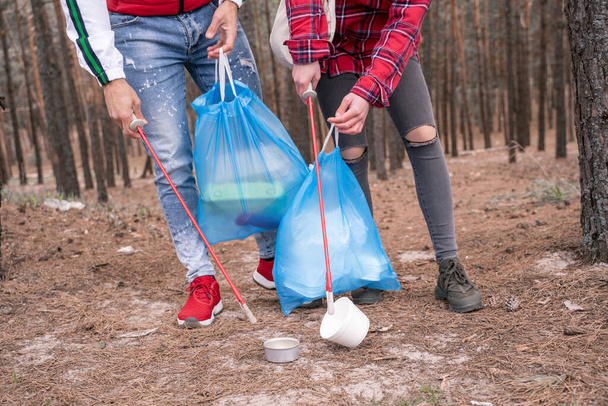 καλλιεργημένη άποψη του ζευγαριού με σακούλες σκουπιδιών μαζεύοντας σκουπίδια με εργαλεία αρπαγής στο δάσος  - Φωτογραφία, εικόνα