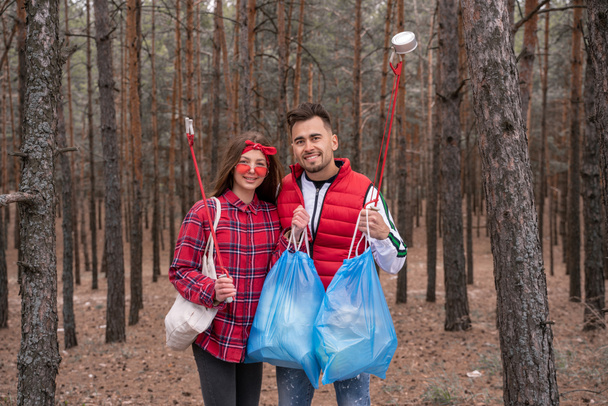 happy couple with trash bags holding pick up tools in forest  - Photo, Image