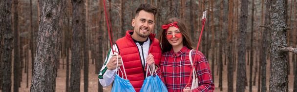 feliz pareja con bolsas de basura sosteniendo recoger herramientas en el bosque, pancarta - Foto, Imagen