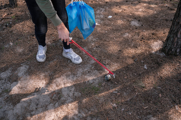 Ausgeschnittener Blick auf freiwillige Helfer, die Werkzeug in der Nähe von Müll im Wald aufheben  - Foto, Bild