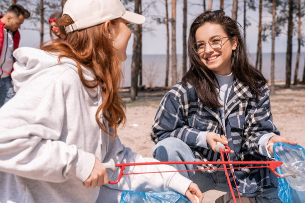 felici giovani donne con afferratori raccogliendo spazzatura al di fuori  - Foto, immagini