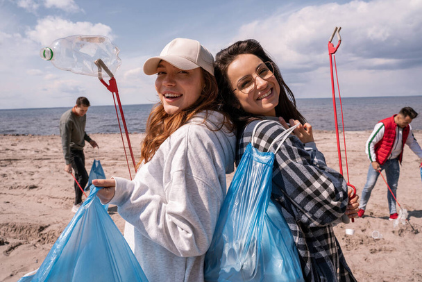 felici giovani donne con afferratori e sacchetti della spazzatura fuori  - Foto, immagini