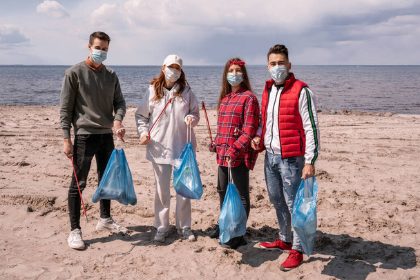 giovani donne e uomini in maschere mediche che tengono sacchi della spazzatura e afferra all'esterno, raccogliere il concetto di spazzatura  - Foto, immagini