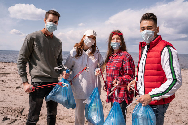 Junge Freiwillige in medizinischen Masken mit Müllsäcken und Greifern vor der Tür holen Müll ab  - Foto, Bild