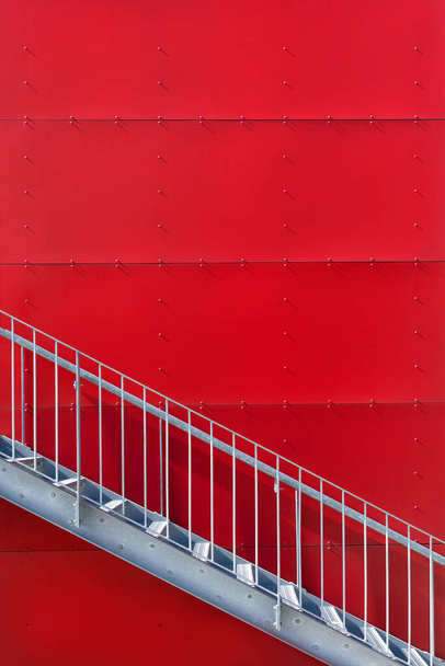 Escalera de metal al aire libre frente a una pared roja, revestida con grandes paneles cuadrados - Foto, Imagen