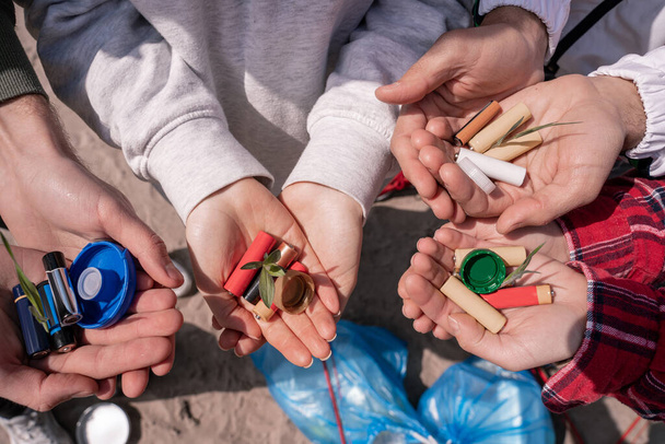 cropped view of volunteers holding batteries, bottle caps and green plants in hands  - Photo, Image