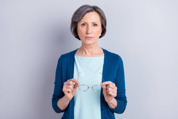 Photo portrait of serious senior woman keeping glasses wearing blue cardigan isolated on grey color background copyspace - Фото, зображення