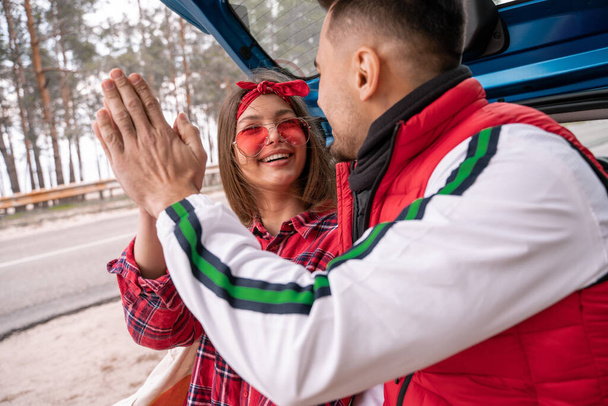 gelukkig vrouw glimlachen terwijl het geven van high five met man in de buurt van auto - Foto, afbeelding